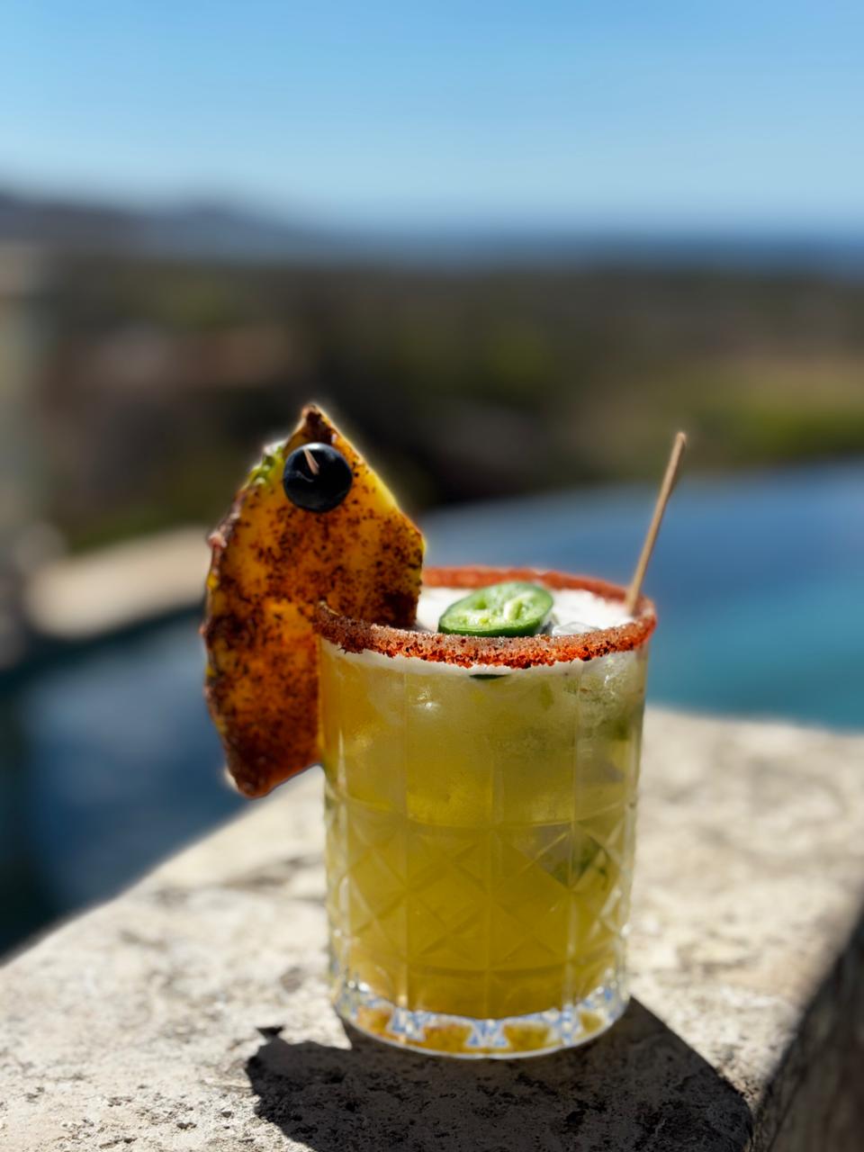 Coctel de piña con jalapeño y borde de chile, frente a una piscina infinita